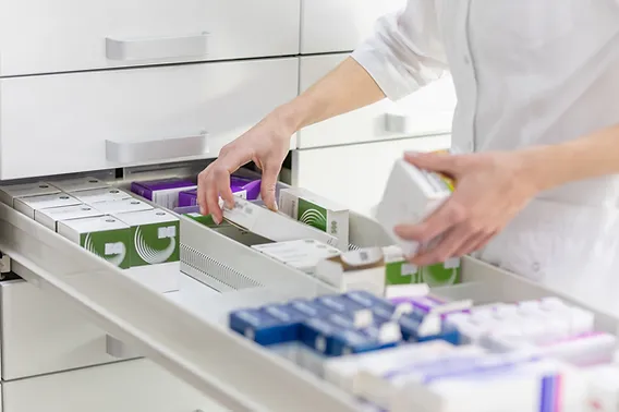 Persona con bata blanca organizando cajas de medicamentos en un cajón — formación para el empleo
