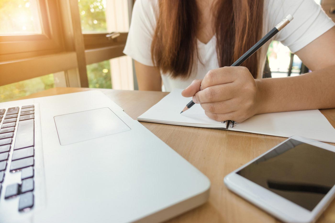 Mano escribiendo en un cuaderno junto a un portátil y un móvil — cursos online