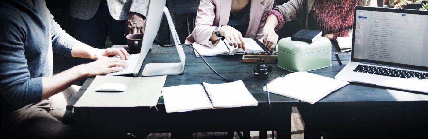 Mesa compartida con ordenadores, cuadernos y manos trabajando en equipo, cursos online