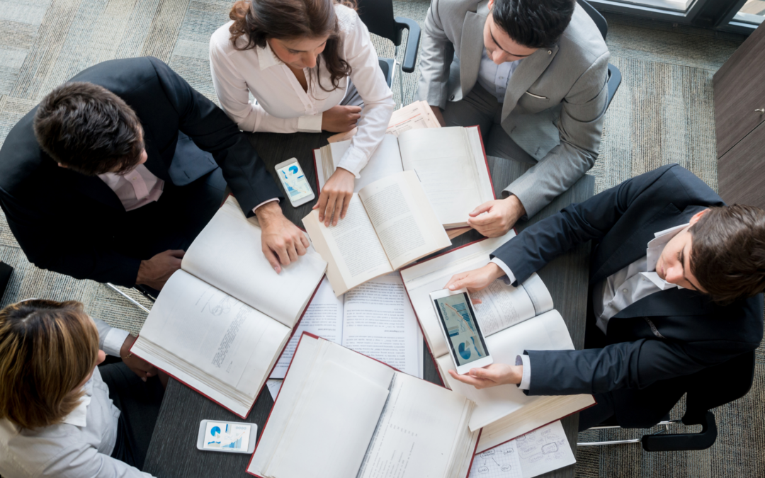 Grupo de cinco profesionales revisando libros y dispositivos electrónicos en una mesa, cursos online