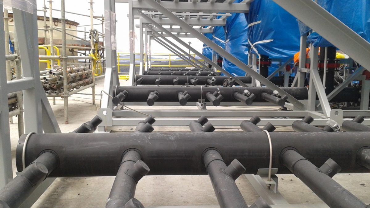 Colector de tuberías negras con salidas en ángulo sobre estructura metálica, mantenimiento industrial