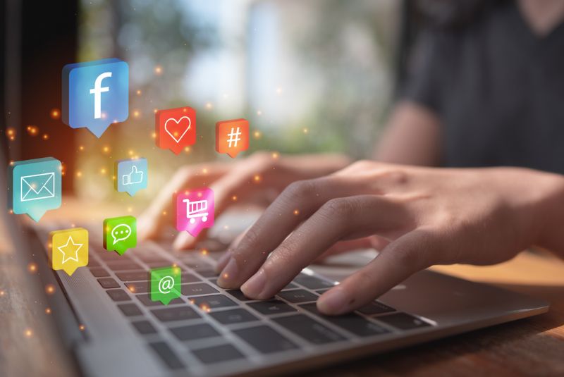 Manos tecleando en un portátil con iconos flotantes de redes sociales, cursos online