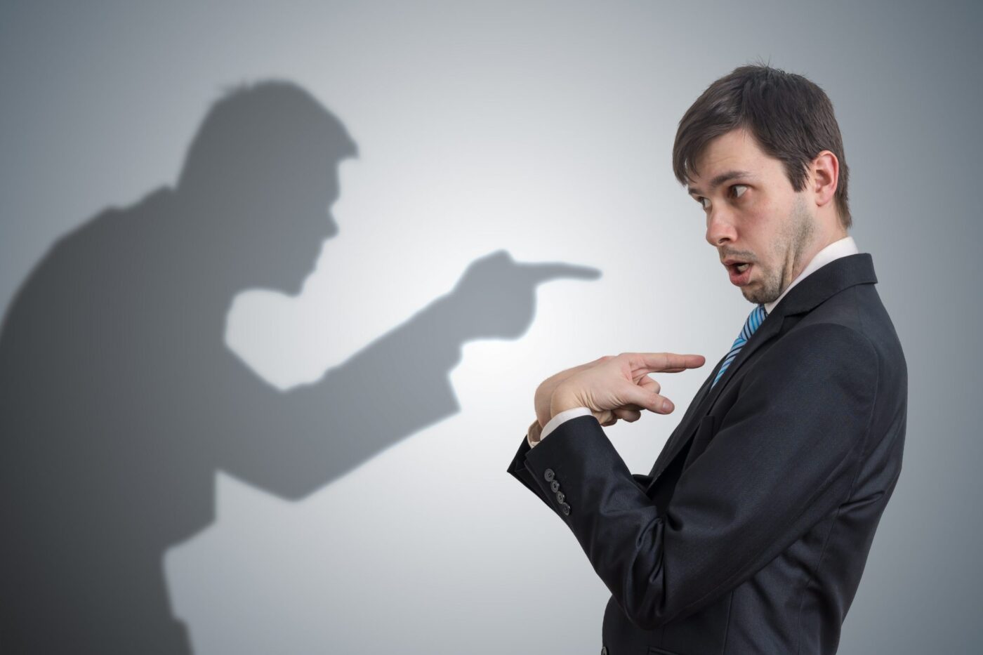 Hombre de traje sorprendido señalándose mientras una sombra lo acusa — formación para el empleo