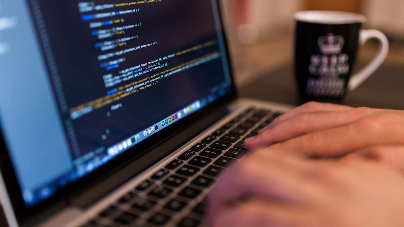 Manos tecleando código en un portátil, taza al fondo — cursos online