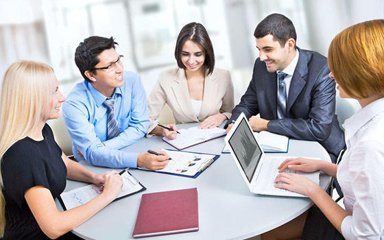 Cinco profesionales reunidos alrededor de una mesa con portátil y documentos, formación para el empleo