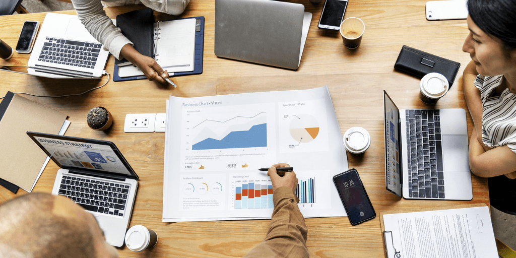 Mesa de reunión con portátiles, gráficos impresos y manos señalando datos, cursos online