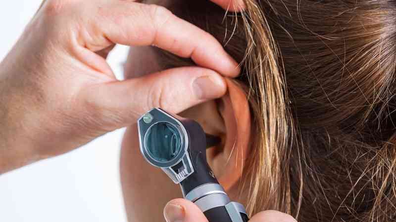 Mano separando la oreja mientras un otoscopio examina el conducto auditivo, cursos online