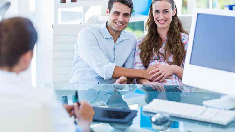 Pareja sonriente en consulta con asesora; mujer embarazada, formación a medida