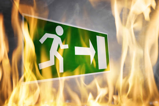 Señal de salida de emergencia verde con pictograma y flecha, rodeada de llamas (cursos sector industrial)