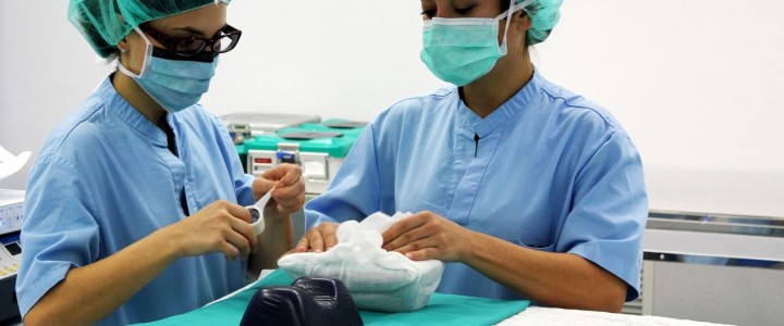 Dos profesionales sanitarias con mascarilla y gorro manipulando un objeto envuelto sobre una mesa clínica — formación para el empleo