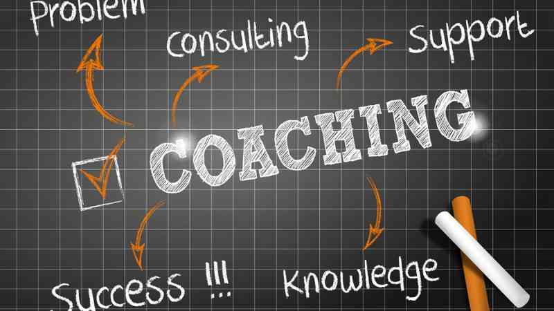 Pizarra cuadriculada con la palabra 'COACHING' en tiza, flechas y palabras relacionadas; formación a medida