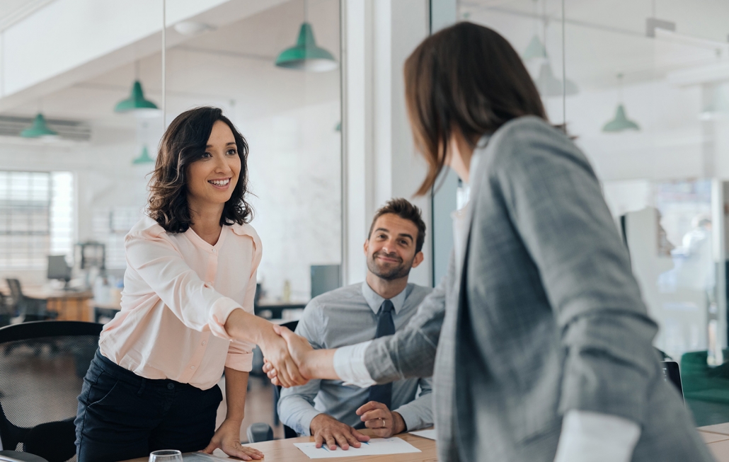 Mujer joven estrechando la mano con otra persona en una sala de reuniones, formación para el empleo