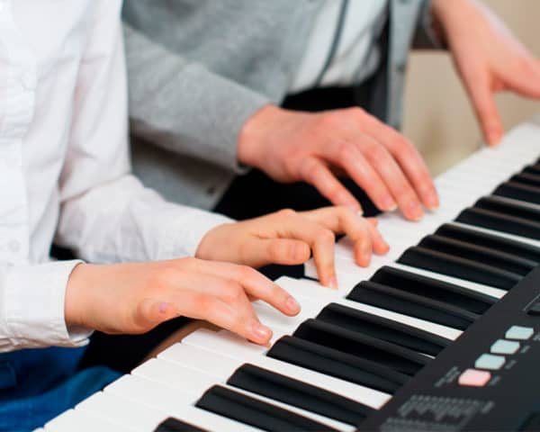 Manos de adulto y niño tocando un teclado electrónico en clase, formación a medida