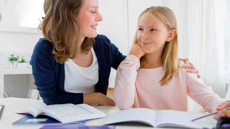 Mujer tutora ayudando a una niña con libros sobre la mesa, formación a medida