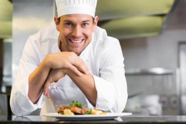 Cocinero sonriente con gorro y uniforme detrás de un plato emplatado — formación para el empleo