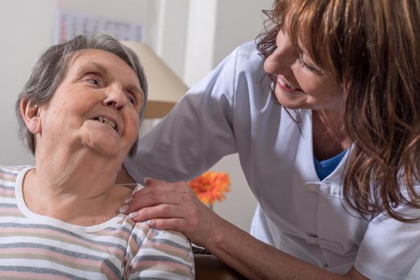 Cuidadora sonriendo coloca la mano en el hombro de una mujer mayor — formación para el empleo