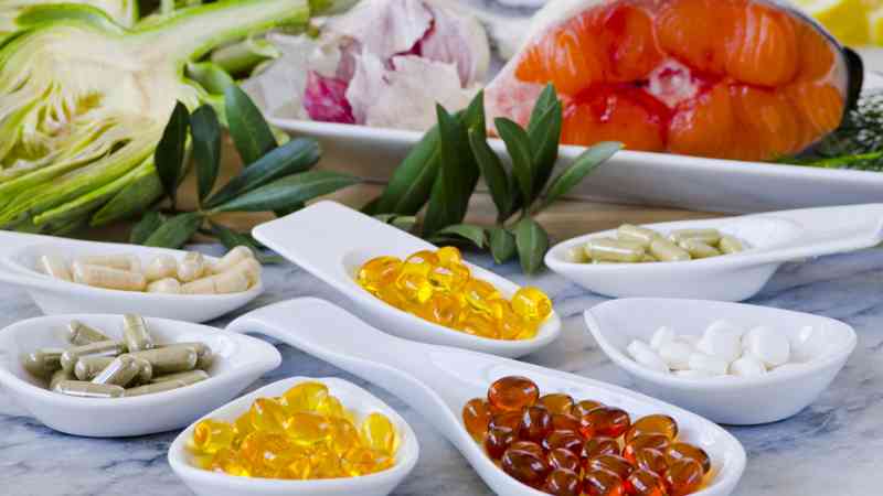Cucharas con cápsulas y comprimidos de suplementos alimenticios, fondo con salmón y hortalizas — cursos online