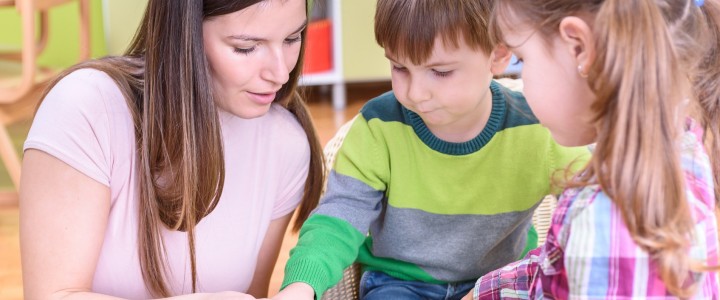 Educadora infantil con dos niños realizando una actividad en mesa, formación a medida