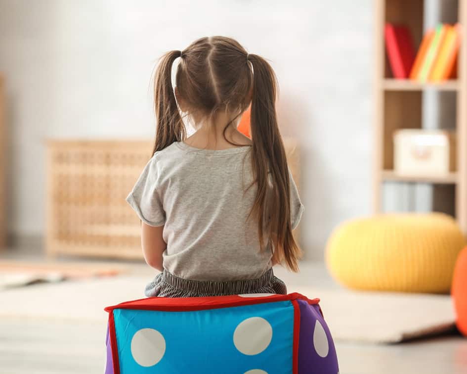 Niña de espaldas con dos coletas sentada sobre un cubo acolchado de colores en una sala — cursos gratuitos