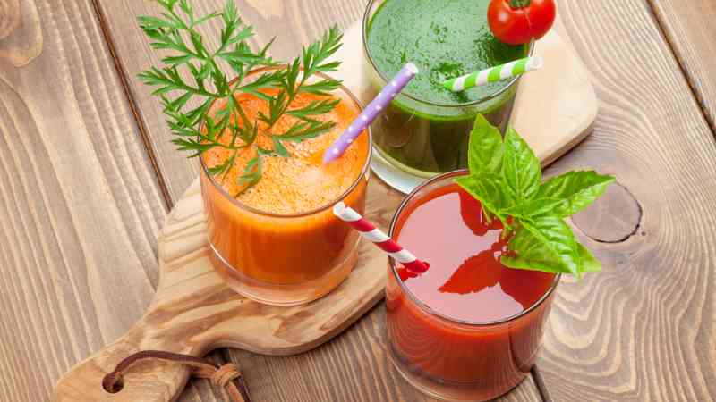 Tres vasos de zumo verde, naranja y rojo con pajitas sobre una tabla de madera (cursos gratuitos)