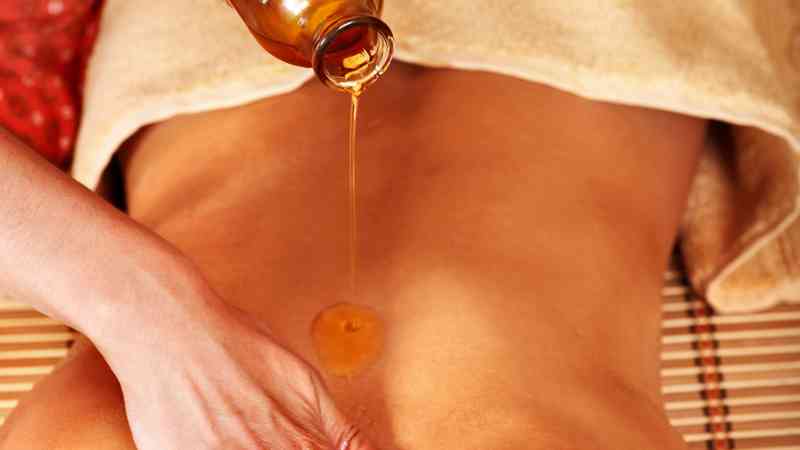 Aceite de masaje vertiéndose sobre el abdomen de una persona tumbada, formación para el empleo