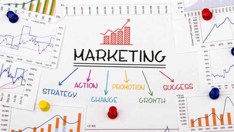 Hoja con 'MARKETING', flechas a conceptos y gráficos clavados, cursos online
