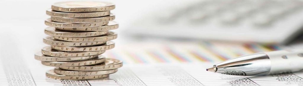 Monedas apiladas sobre documento financiero con bolígrafo — formación para el empleo