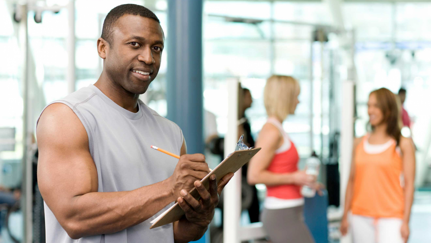 Entrenador en gimnasio con portapapeles y lápiz, formación para el empleo