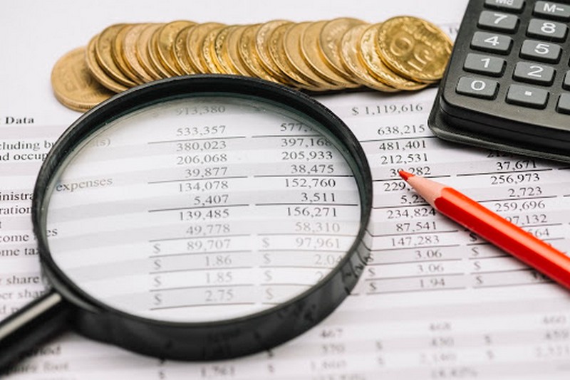 Lupa, monedas y calculadora sobre hoja de cifras — formación para el empleo