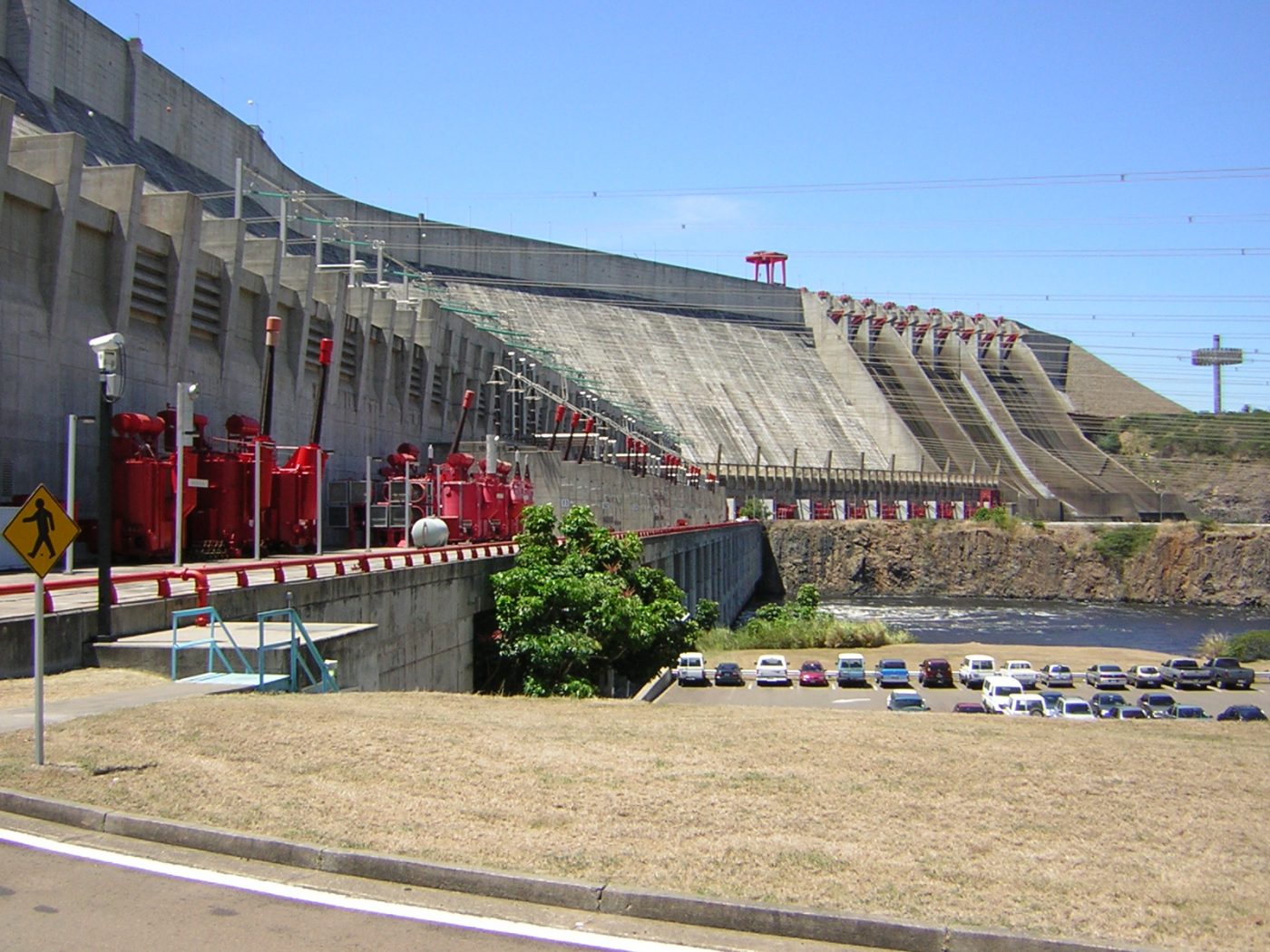 Presa de hormigón con compuertas y maquinaria roja en pasarela, mantenimiento industrial