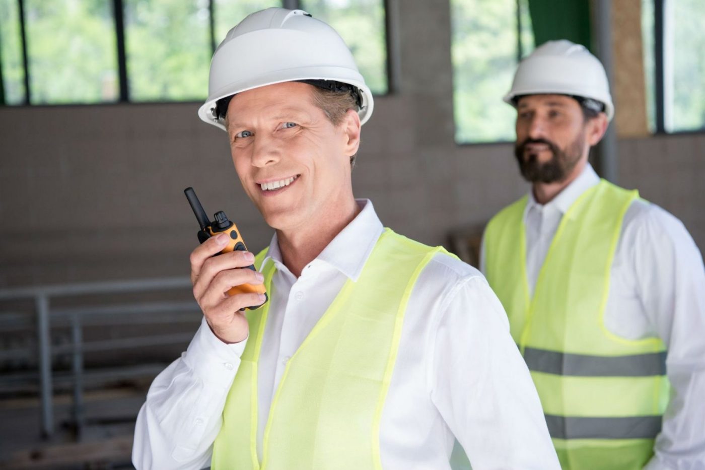 Hombre con casco blanco y chaleco amarillo hablando por walkie-talkie, cursos sector industrial
