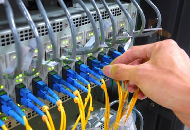 Panel de fibra óptica con conectores azules y cables amarillos, mano ajustando un cable — cursos sector industrial