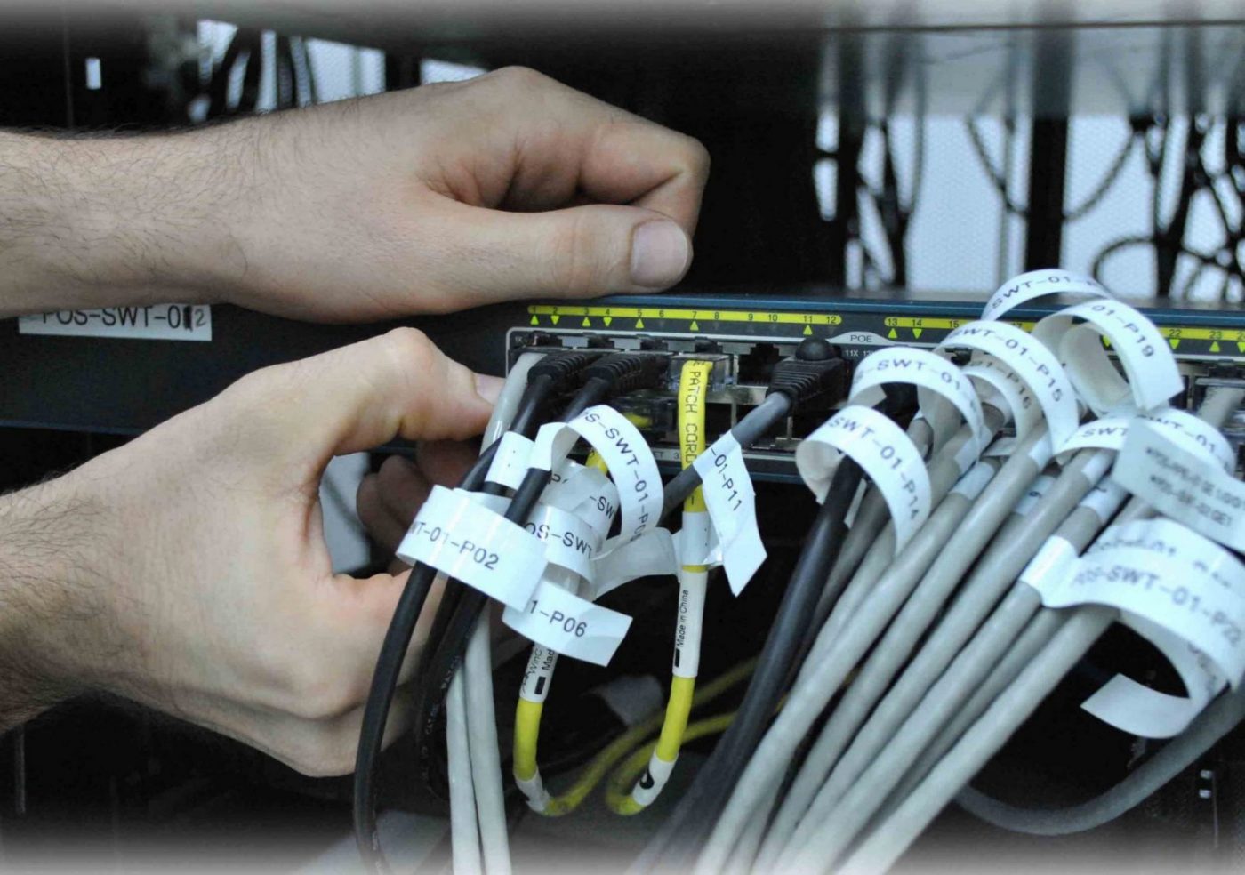 Manos conectando cables Ethernet etiquetados en un switch (cursos con prácticas en empresa)