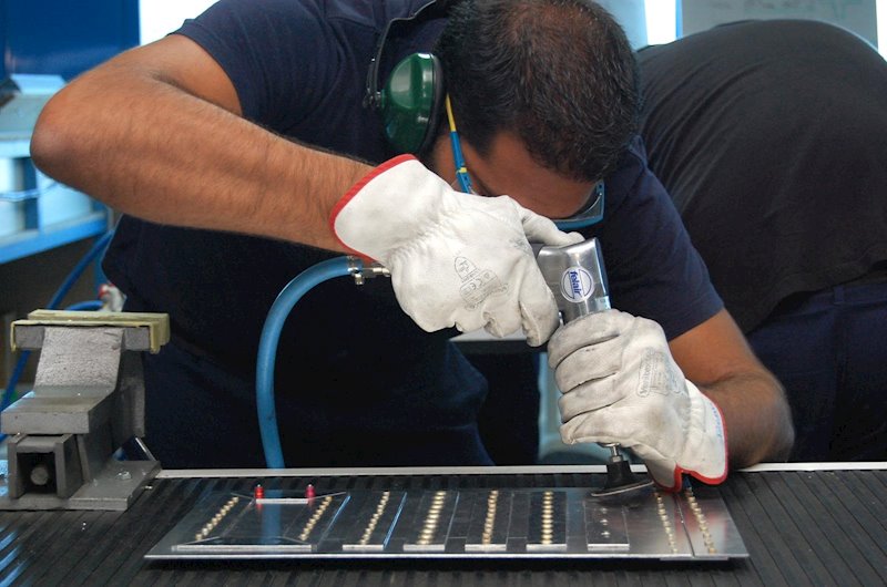 Operario con guantes y protección auditiva usando herramienta neumática sobre una pieza de calderería industrial