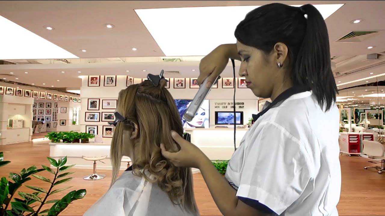 Estilista alisando el cabello de una clienta en salón — formación para el empleo
