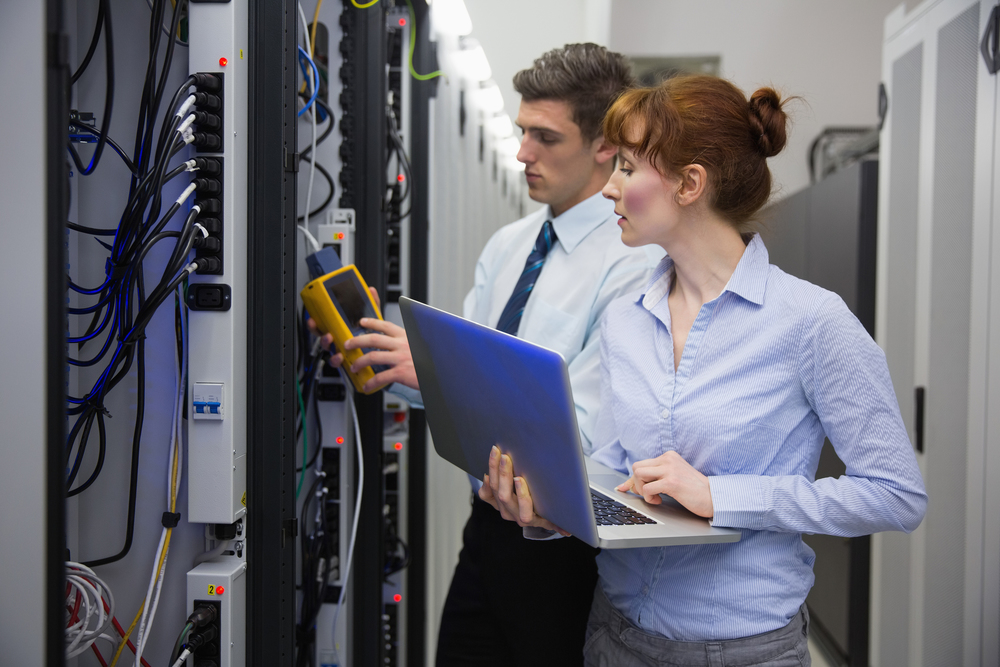 Técnicos revisando un rack de servidores con portátil y analizador amarillo — cursos online
