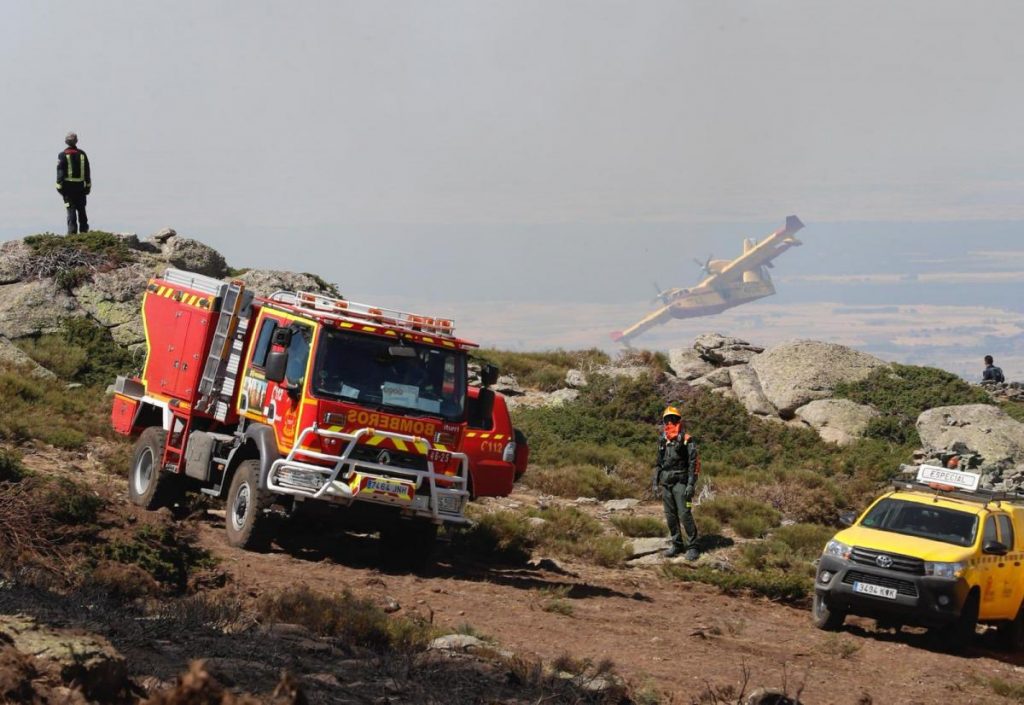 Bomberos junto a camión de bomberos en terreno rocoso con un Canadair en vuelo, formación para ayuntamientos