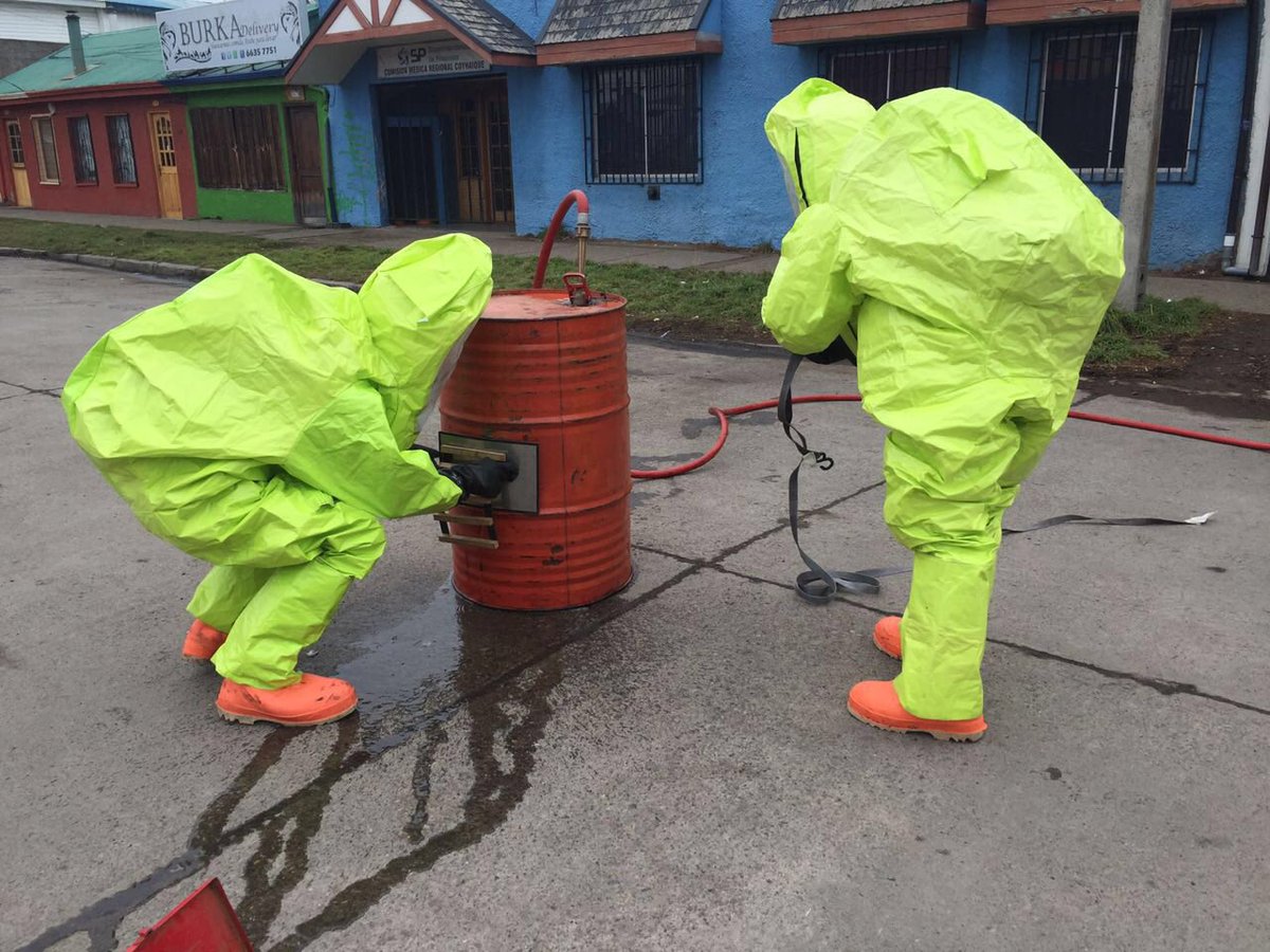 Dos personas con trajes protectores fluorescentes manipulando un bidón rojo en la calle, cursos sector industrial