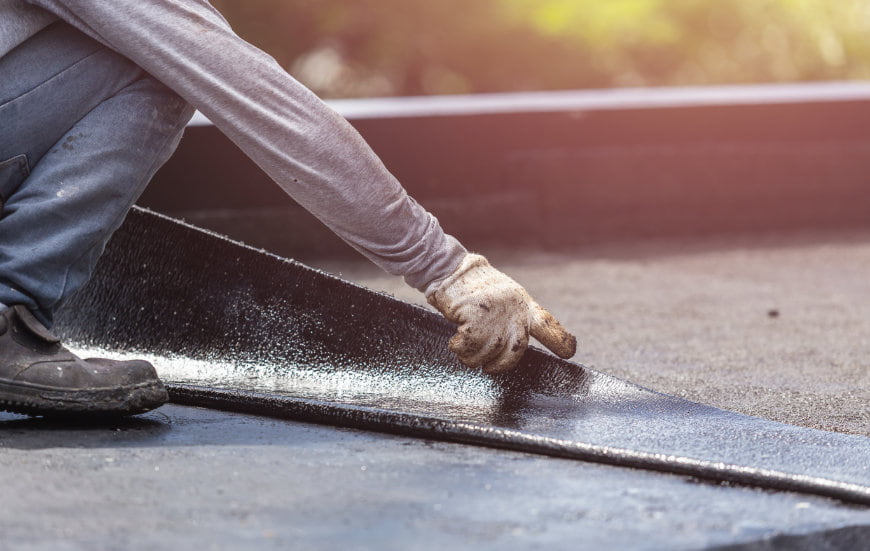 Trabajador aplicando lámina asfáltica sobre pavimento, mantenimiento industrial