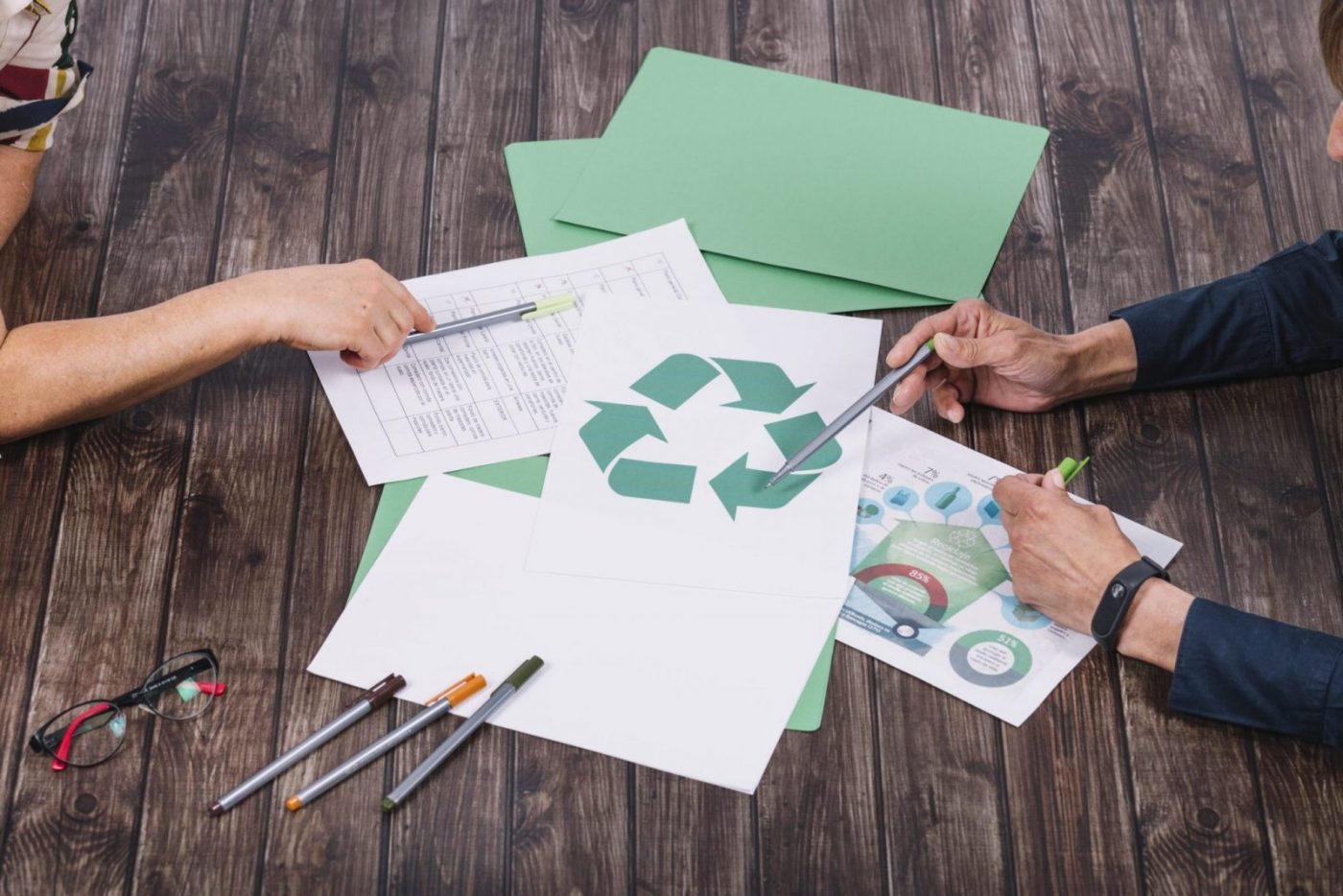Manos señalando un símbolo de reciclaje sobre documentos y carpetas verdes, formación para asociaciones