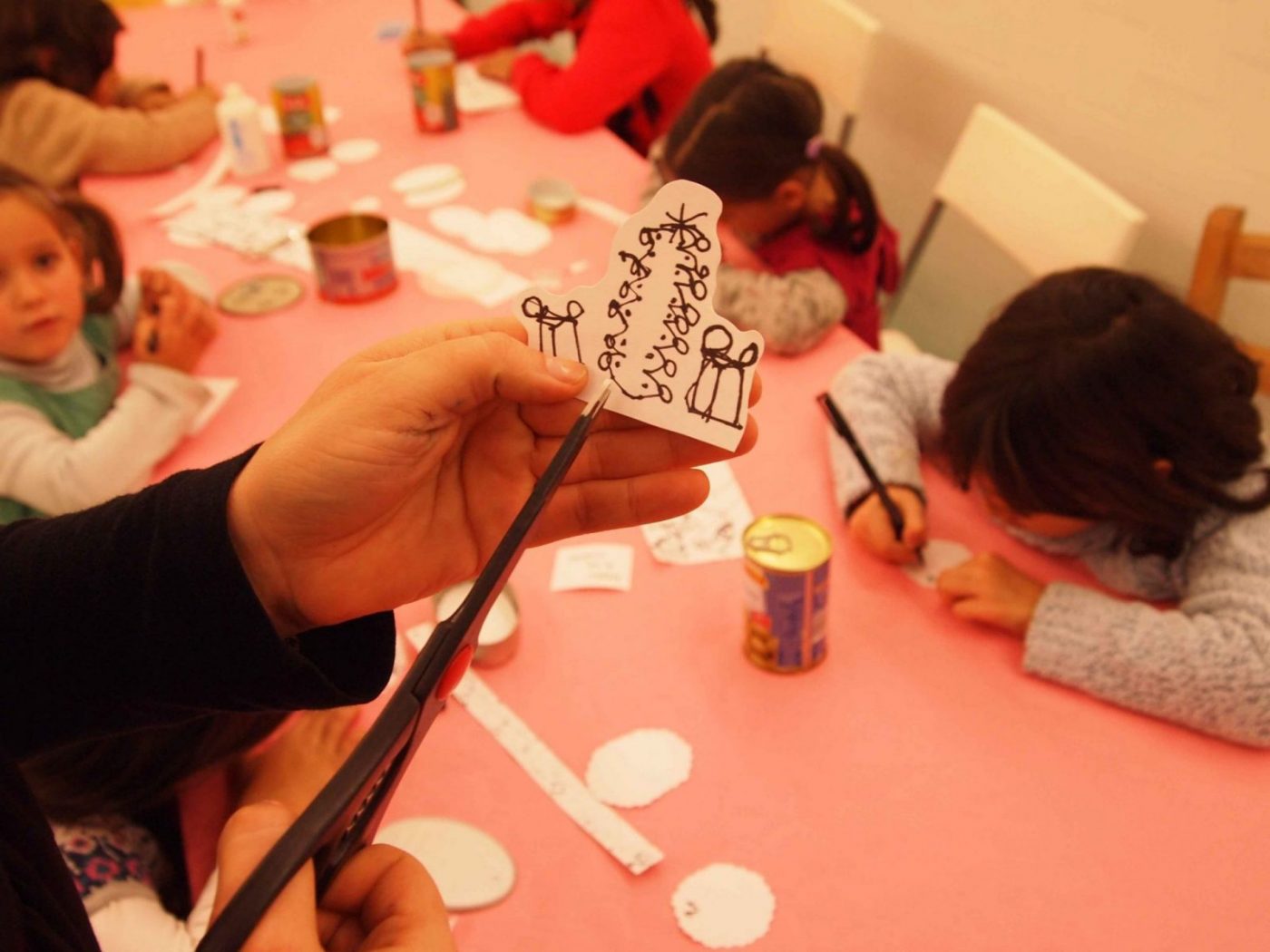 Mano recortando figura de papel con dibujo de árbol y regalos en taller infantil — formación para asociaciones