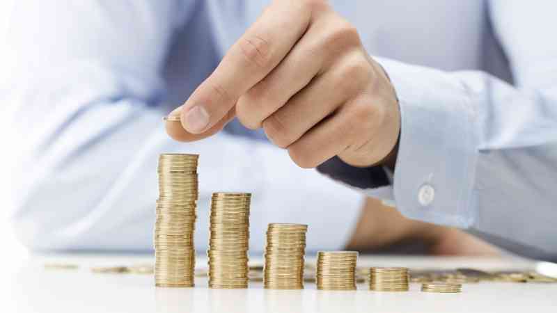 Mano colocando una moneda sobre pilas de monedas en aumento, cursos online