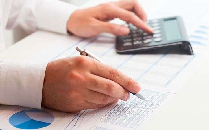 Manos anotando cifras en hojas con tablas y gráfico junto a una calculadora — formación para el empleo