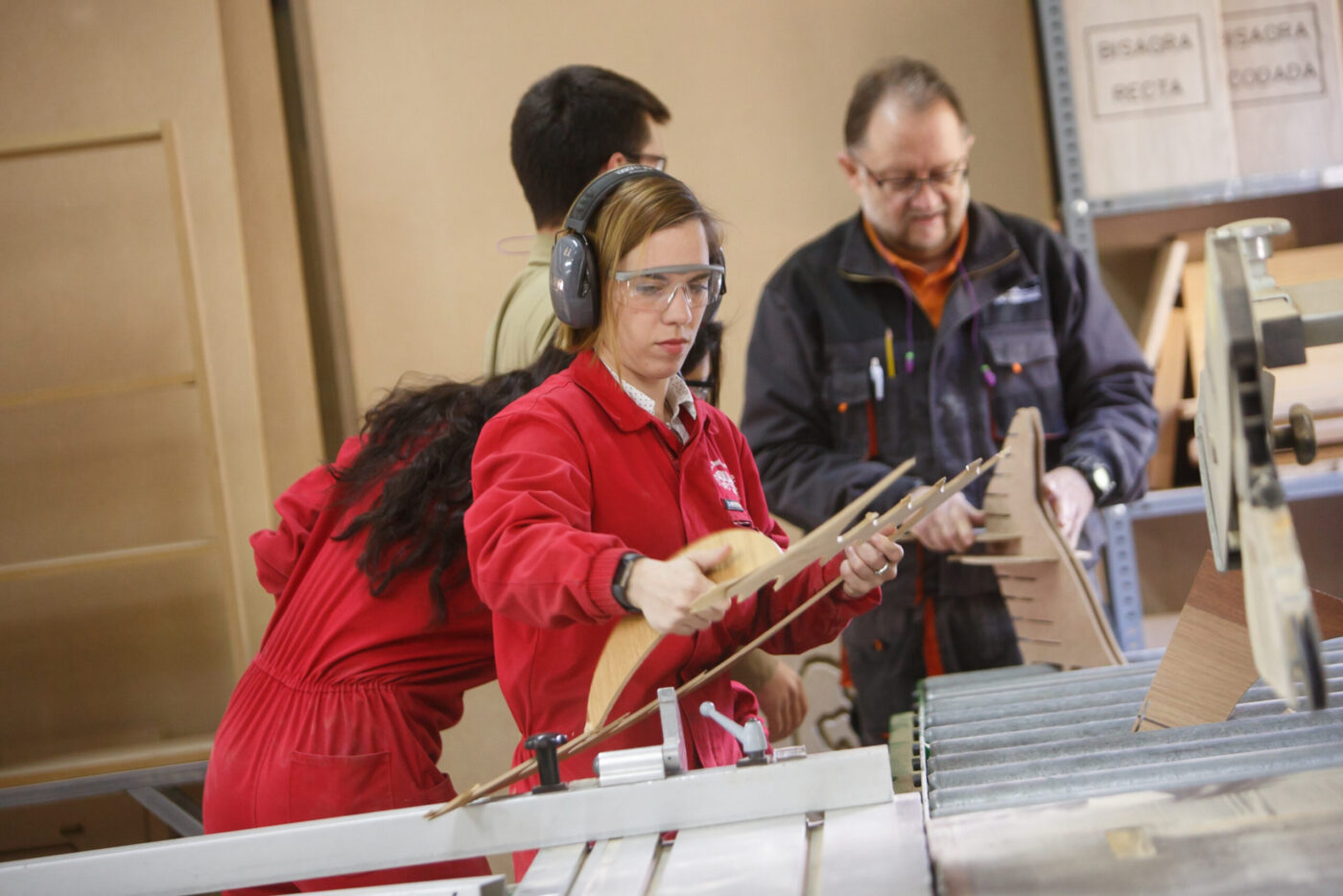 Operaria con gafas y protección auditiva manejando piezas de madera en una máquina, cursos de maquinaria