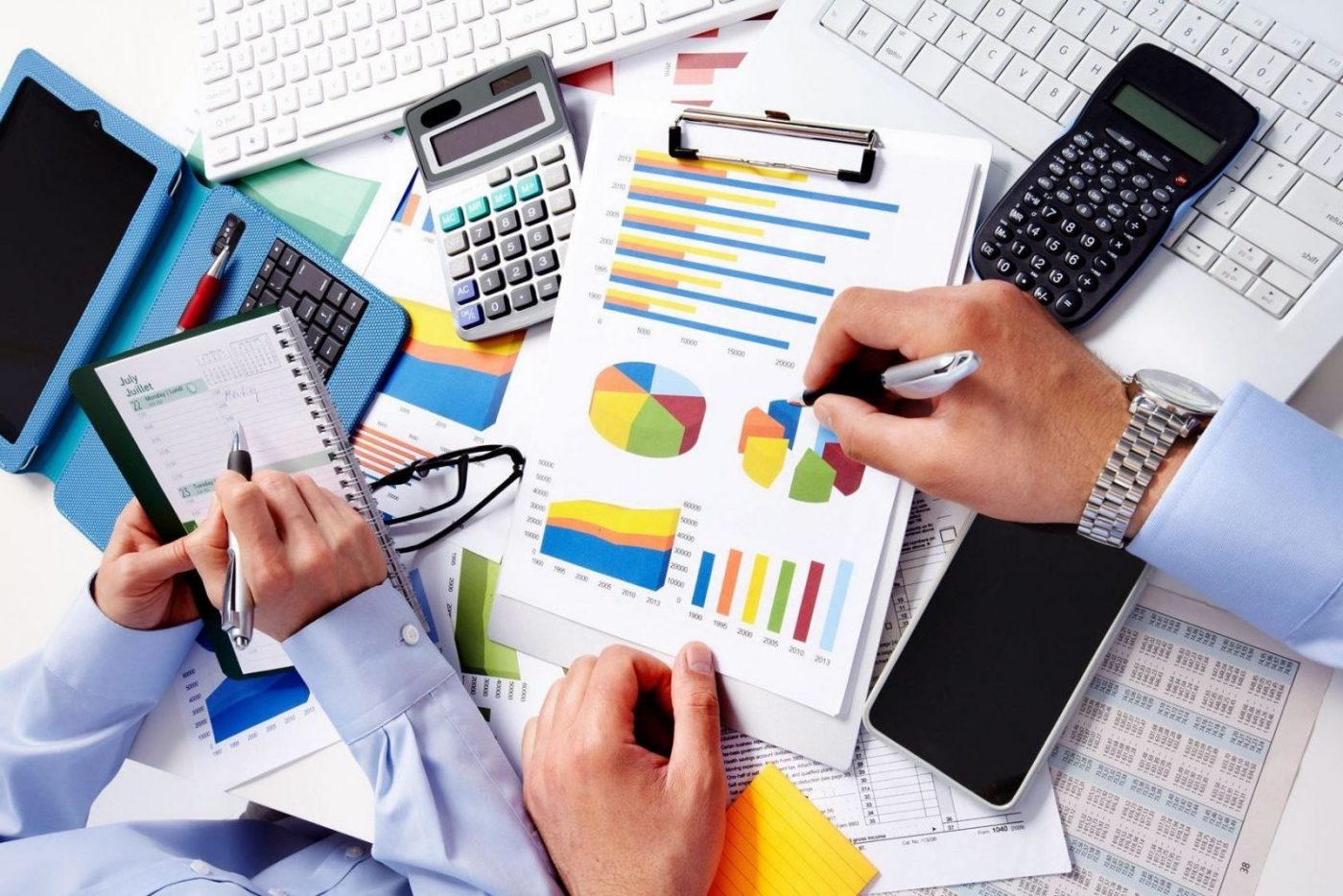 Manos analizando gráficos impresos con calculadora, tablet y bloc de notas, cursos online