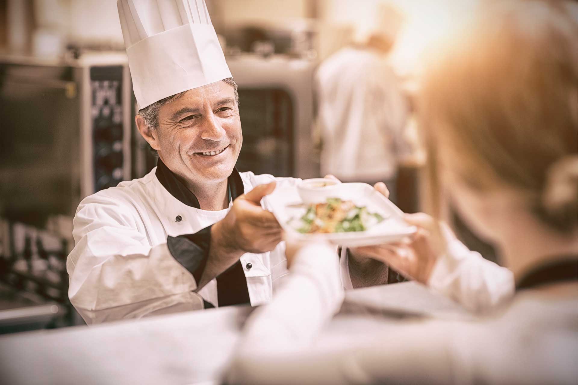 Cocinero con gorro entregando un plato, cursos con prácticas en empresa