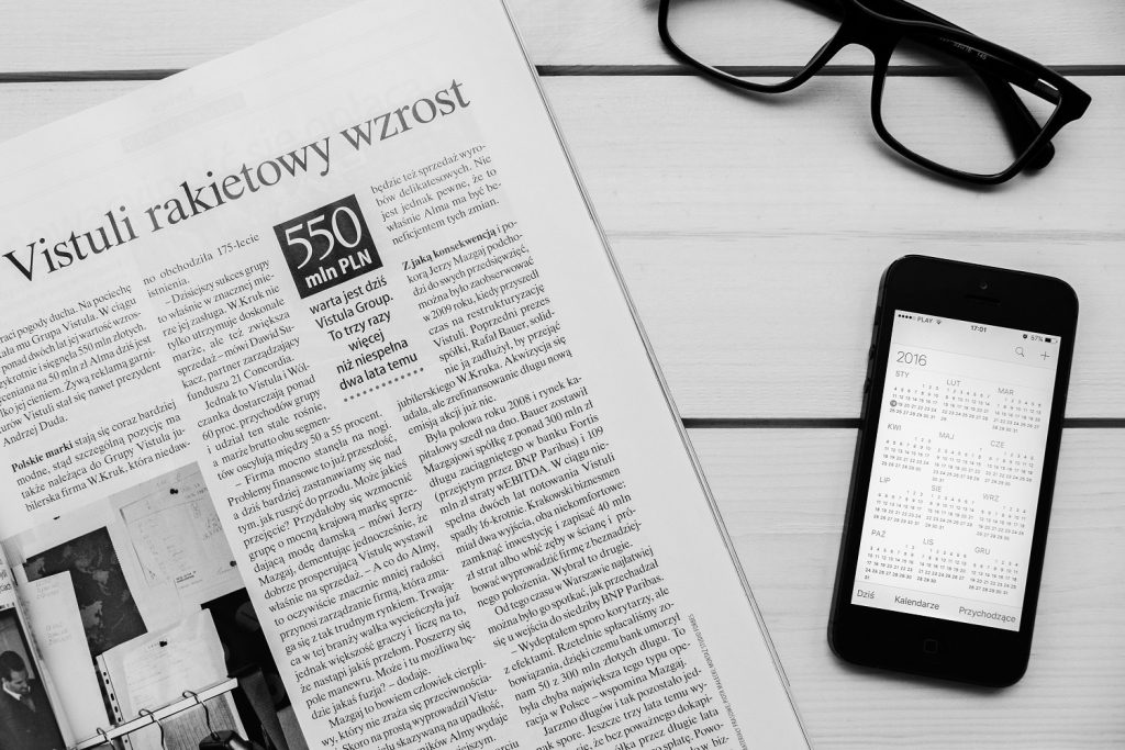 Periódico abierto con titular en polaco, smartphone con calendario y gafas sobre mesa, cursos online