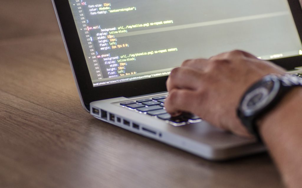 Mano tecleando código en un portátil con pantalla de CSS — cursos online