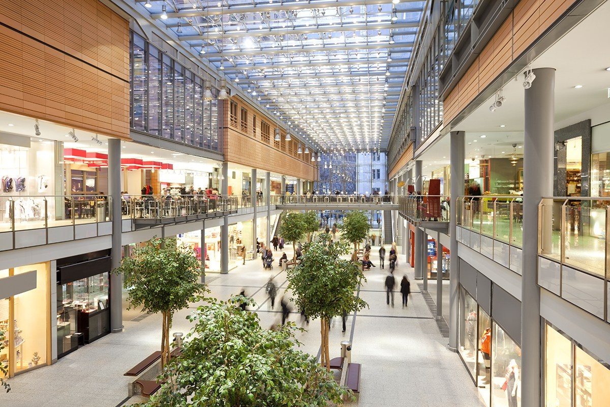 Pasillo central de un centro comercial moderno con tiendas en dos plantas y techo acristalado — formación para el empleo