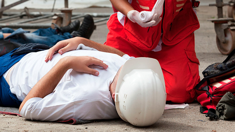 Trabajador inconsciente con casco blanco atendido por un técnico de emergencias en obra — cursos sector industrial